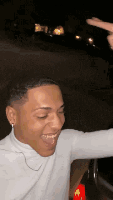 a man wearing a white turtleneck is laughing and giving a thumbs up