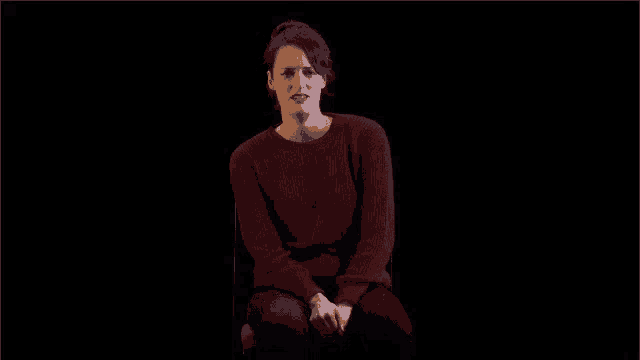 a woman in a red sweater is sitting in front of a black background and says the drama of it