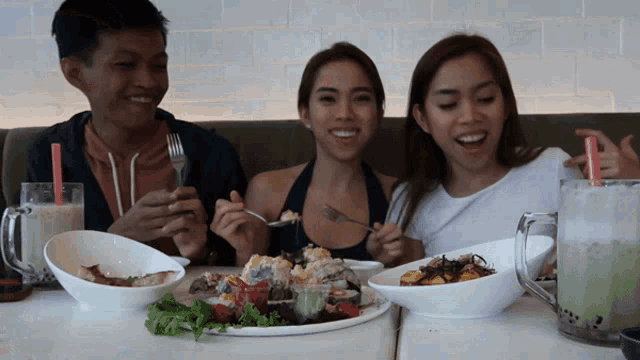 three people are sitting at a table eating food and drinking