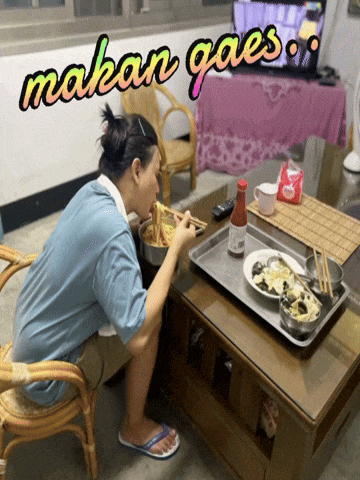 a man is sitting at a table eating food with the words makan gaes written above him