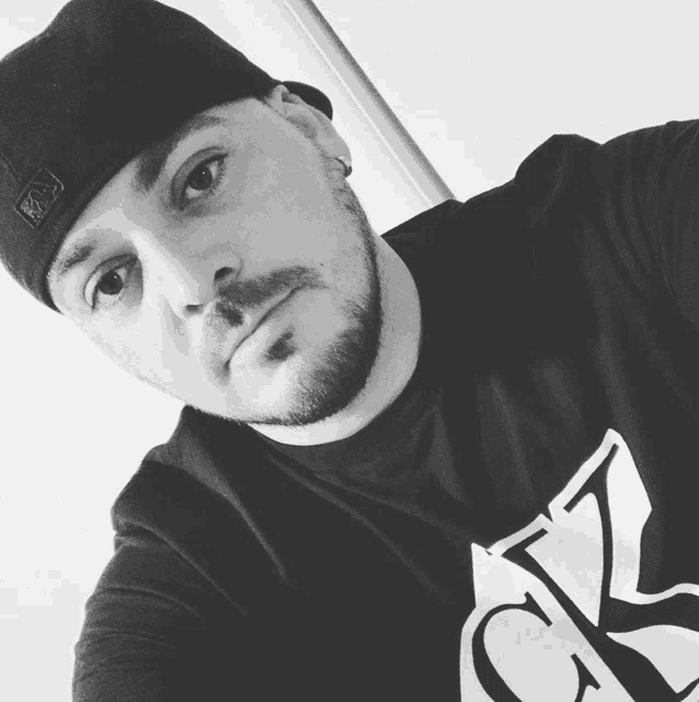 a man with a beard wearing a hat and a shirt with the letter k on it