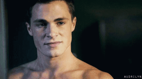 a shirtless man is smiling and looking at the camera while standing in a dark room .