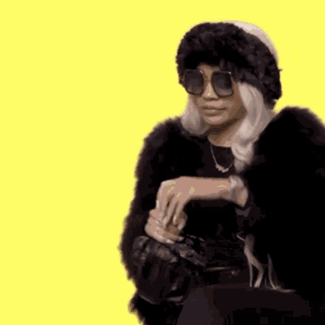 a woman wearing sunglasses , a fur coat , and a hat is holding a purse .