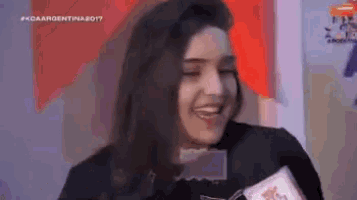 a woman is smiling while holding a piece of paper in front of her face .