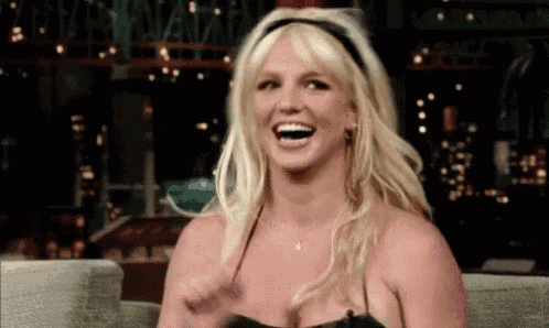 britney spears is laughing while sitting in a chair and wearing a headband .