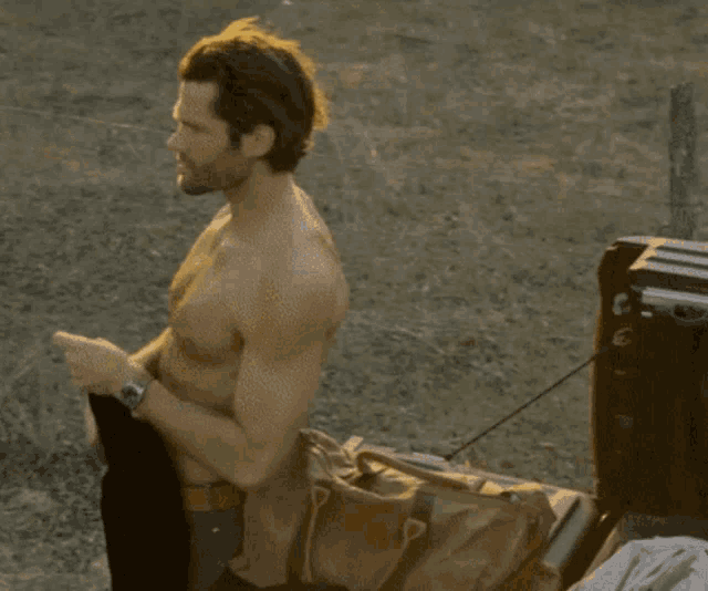 a man without a shirt is standing next to a suitcase