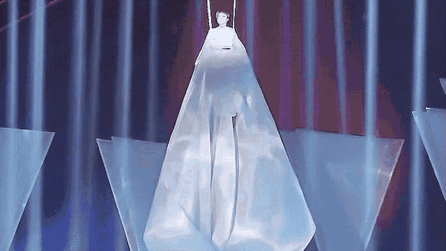 a woman in a white dress is hanging from a rope on a stage