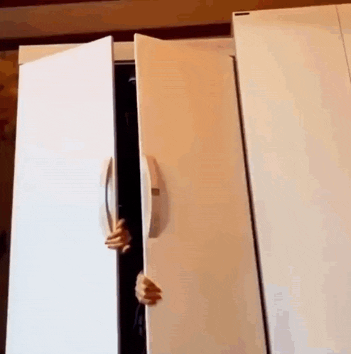 a person is peeking out of a white refrigerator .