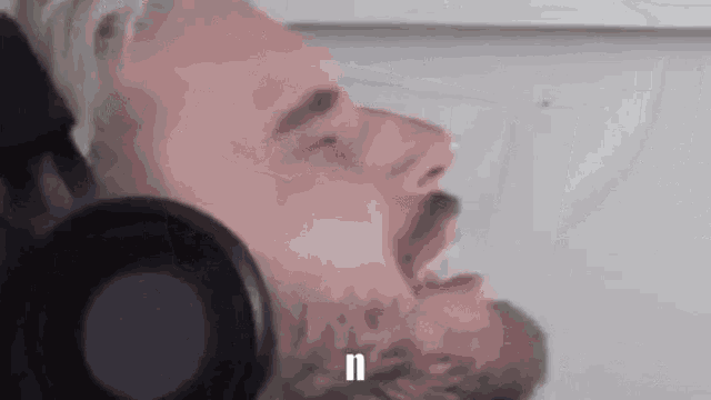 a man with a beard is wearing headphones and making a funny face with his mouth open .