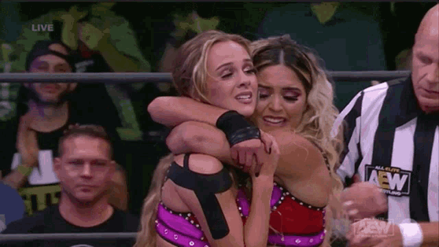 two women are hugging each other in a wrestling ring while a referee watches .