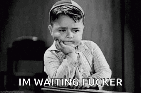 a little boy is sitting at a desk with his hand on his chin and the words `` im waiting fucker '' written on the screen .