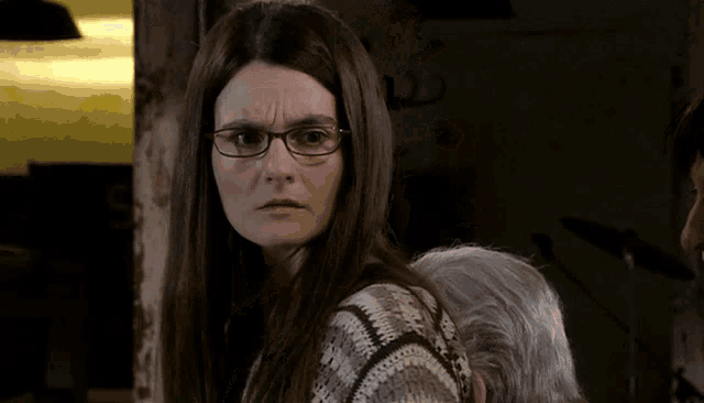 a woman wearing glasses and a sweater looks at the camera