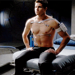 a shirtless man is sitting on a bed with a monitor around his chest