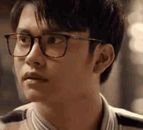 a young man wearing glasses and a striped shirt is looking at something .