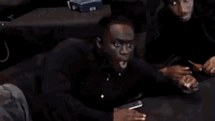 a man is sitting on a couch with his mouth open and his hands folded .