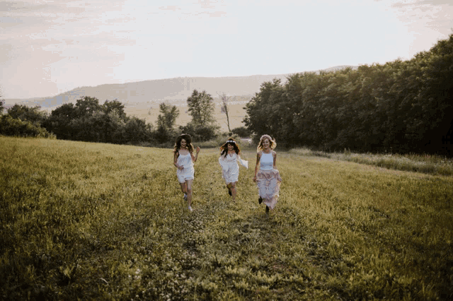 three women in white dresses are running in a field