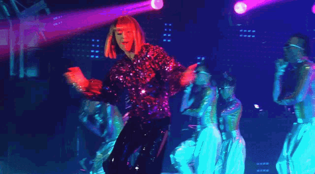 a woman is singing into a microphone while a group of dancers stand behind her