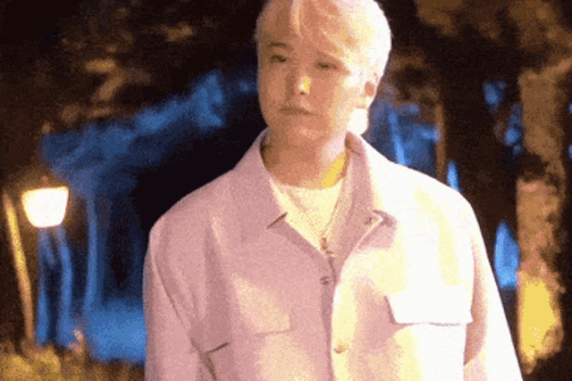 a young man in a purple shirt is standing in front of a street light at night .