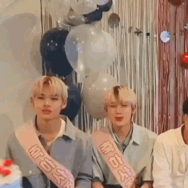 a group of young men are sitting next to each other in front of balloons and a cake .