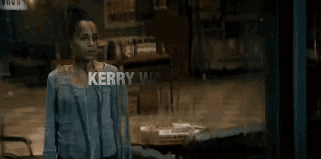 a woman in a blue shirt stands in front of a sign that says kerry washington