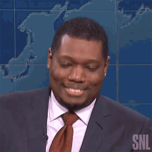 a man in a suit and tie is smiling with the snl logo behind him