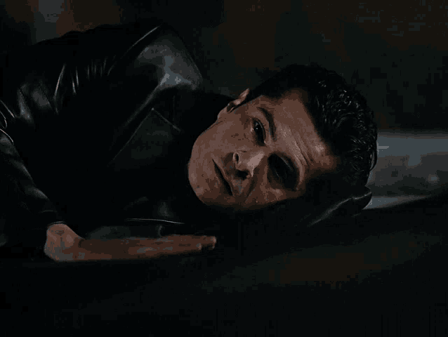a man in a black jacket is laying on the ground