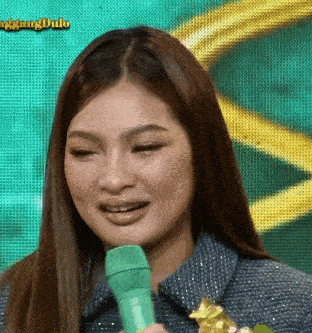 a woman is holding a green microphone and smiling in front of a screen that says ang dula
