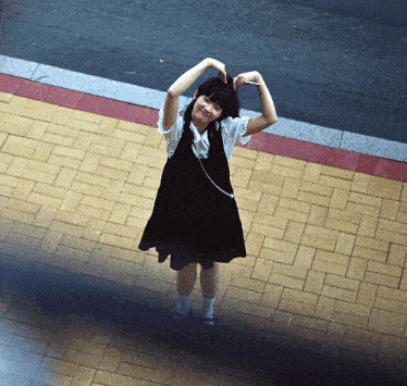 a young girl in a black dress is making a heart shape with her hands