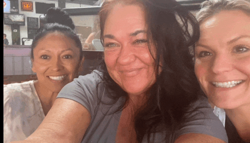 three women are posing for a picture and one of them has a sign on the wall that says ' texas ' on it