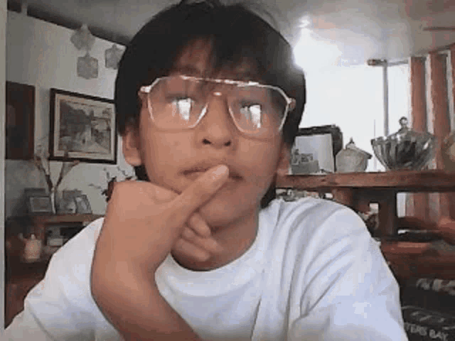 a young boy wearing glasses and a white shirt is thinking