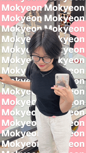 a woman wearing glasses and a black shirt is holding a cell phone in front of a collage of words including mokyeon