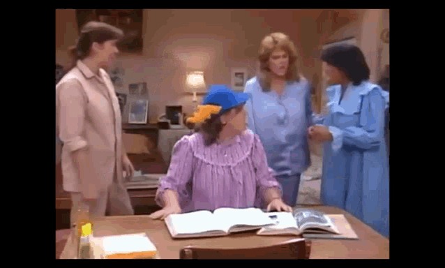 a group of women are sitting at a table with a book and talking .