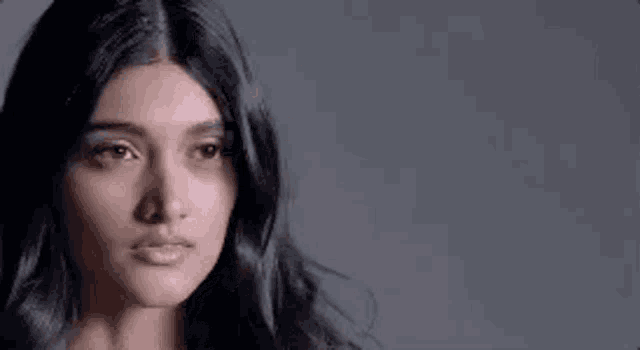a close up of a woman 's face with long black hair and a gray background .