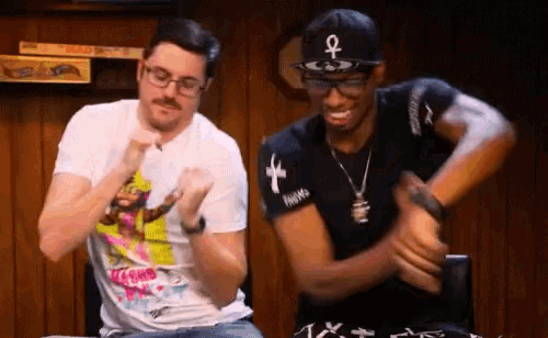 a man wearing a hat with an ankh on it is dancing with another man
