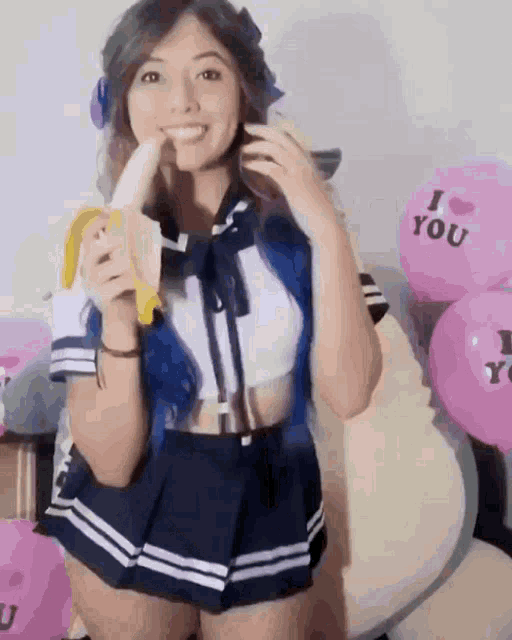 a girl in a school uniform is eating a banana in front of balloons that say i love you