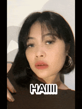 a woman with short hair is wearing hoop earrings and has the word haiii on her chest