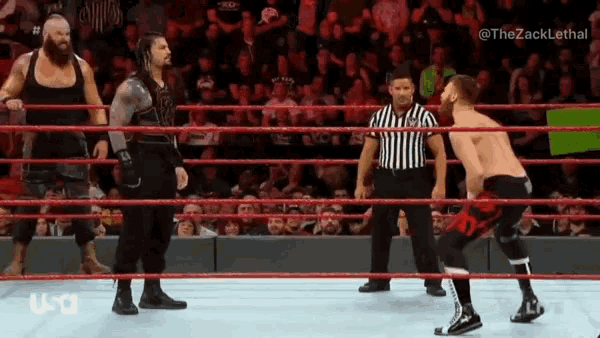 a referee is standing in the middle of a wrestling ring watching two wrestlers wrestling .