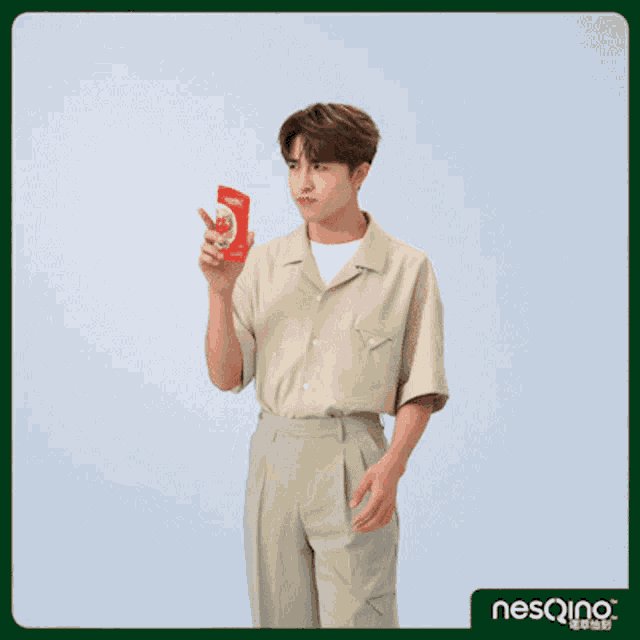 a man in a tan shirt is holding a red box of nesqino