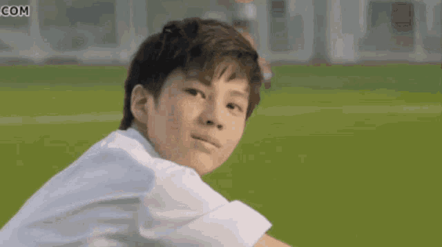 a young boy in a white shirt is smiling and looking at the camera on a field .