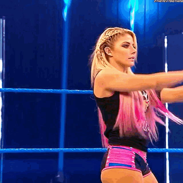 a woman with pink hair is standing in a wrestling ring with her hands in the air