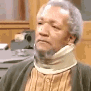 a man wearing a neck brace and a sweater is sitting in front of a camera .