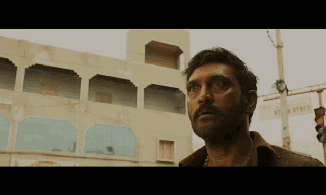 a man with a beard stands in front of a building with a sign on it that says ' r.t. '
