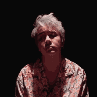 a man with white hair is wearing a floral shirt and looking at the camera .
