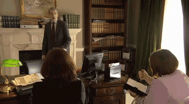 a man in a suit and tie stands in front of a bookshelf with books on it
