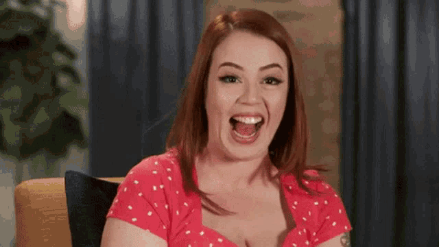 a woman in a red dress is sitting on a couch and making a funny face .