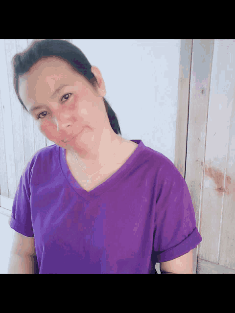 a woman wearing a purple shirt is standing in front of a wall