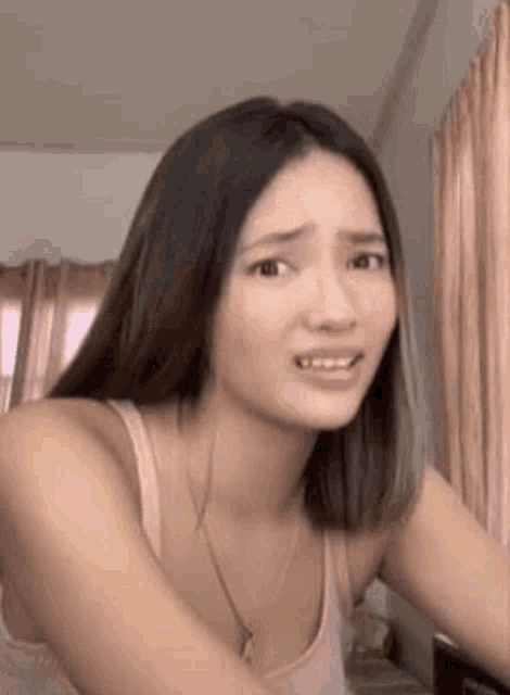 a woman in a tank top is making a funny face in a bedroom .