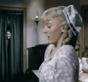 a woman in a blue hat is standing in a room with a green curtain .