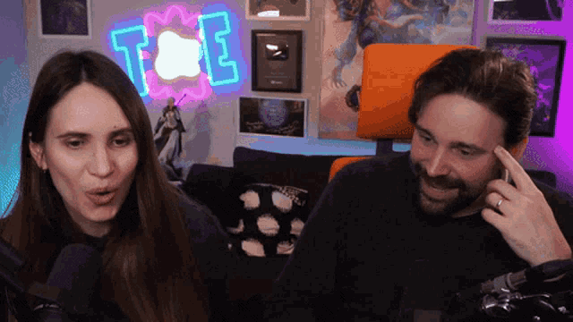 a man and woman are sitting in front of a neon sign that says t & e