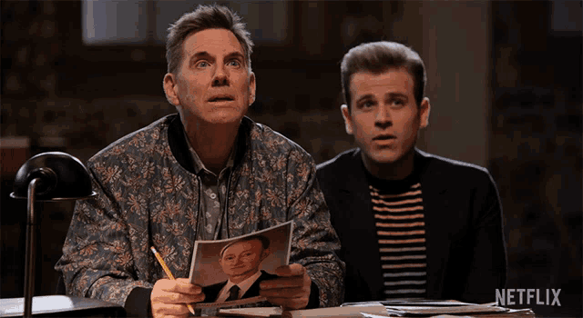 two men are sitting at a table with a netflix logo in the background
